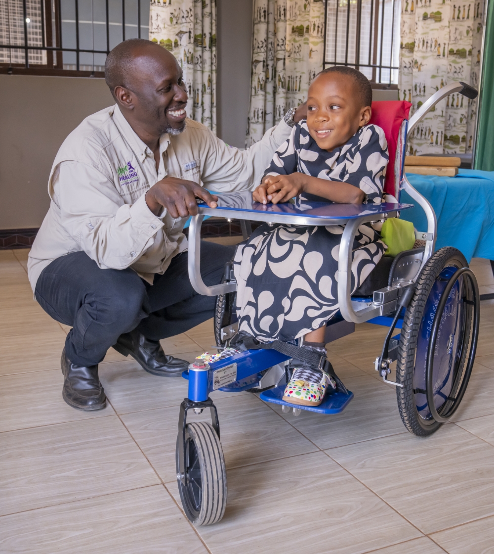 Hope and Healing International Executive Director, Kyalo, smiling next to Rose in her brand new wheelchair.