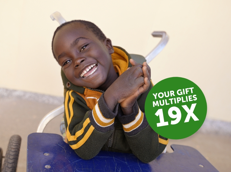 Gerald sitting in a wheelchair smiling. Overlaid text reads 'your gift multiplies 19 times.'