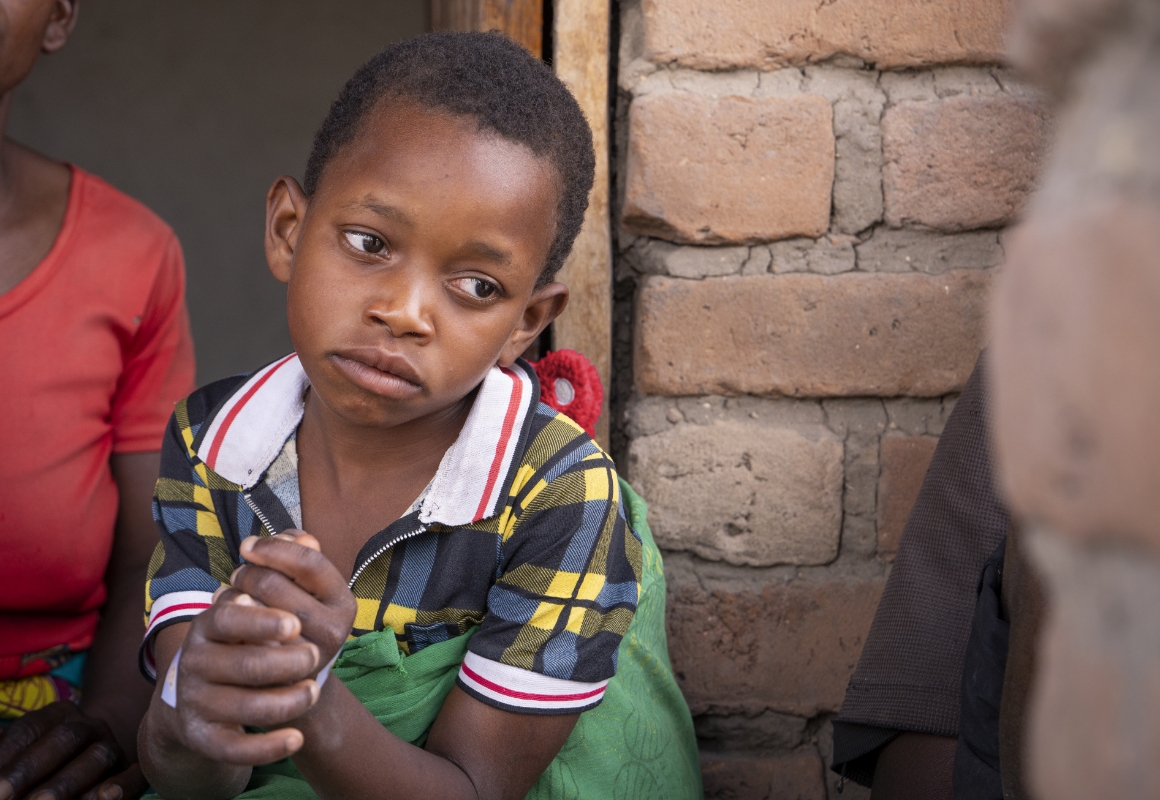 Justina, a young girl, sits in front of her home, gazing sadly off to the side.